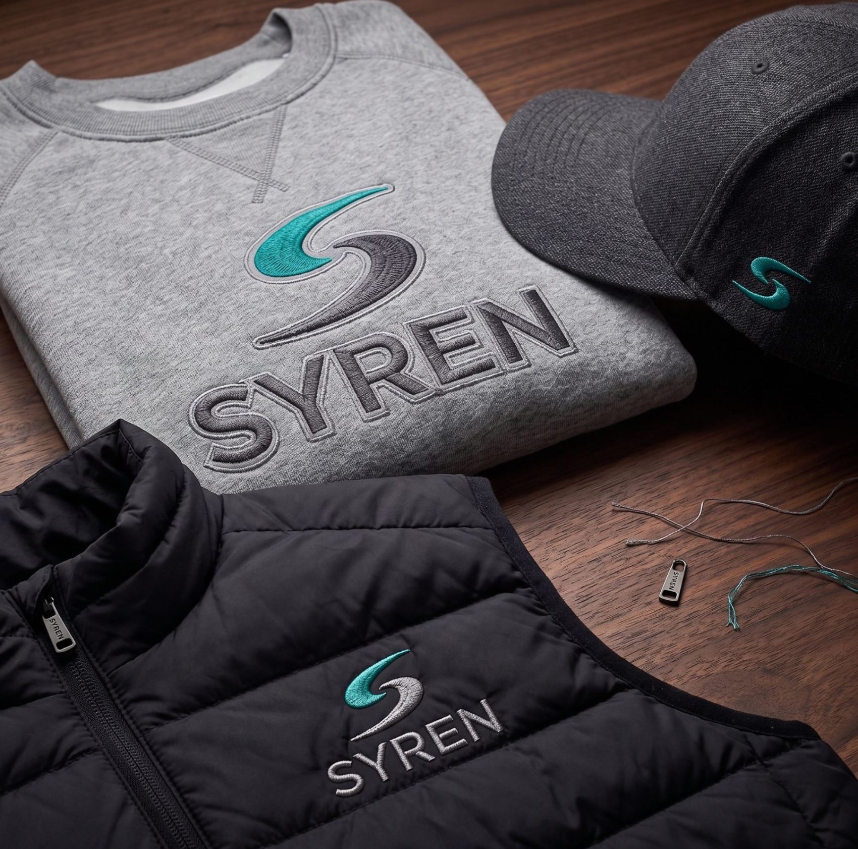 Embroidered SYREN sweatshirt, cap and gilet on a workshop bench